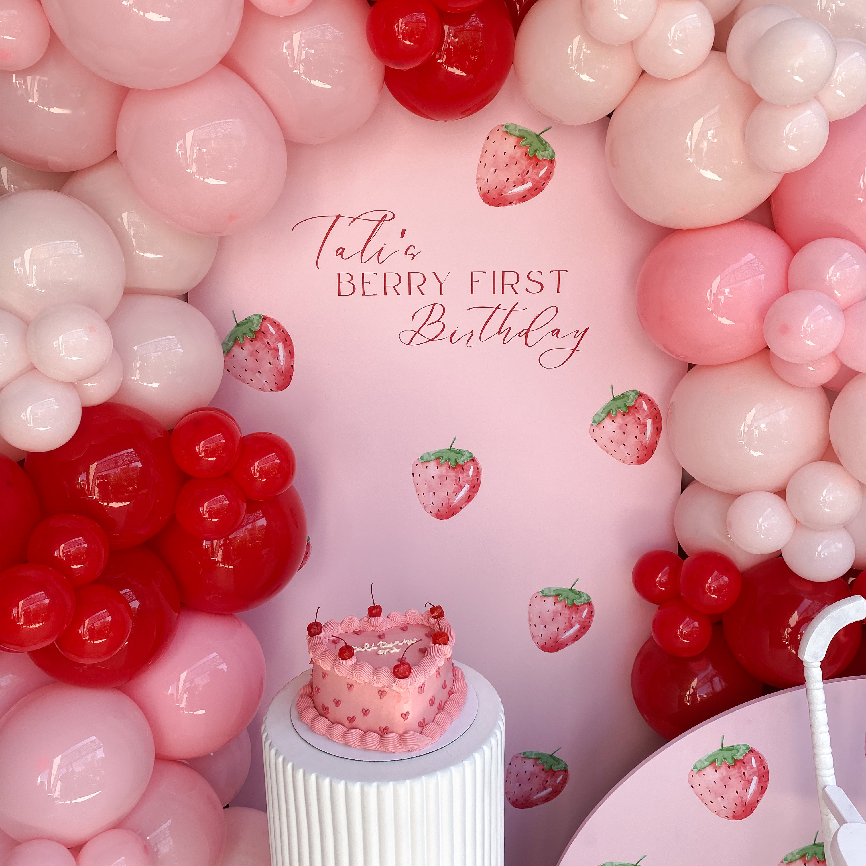 Berry-themed party backdrop with balloons and vinyl signage for first birthday celebration