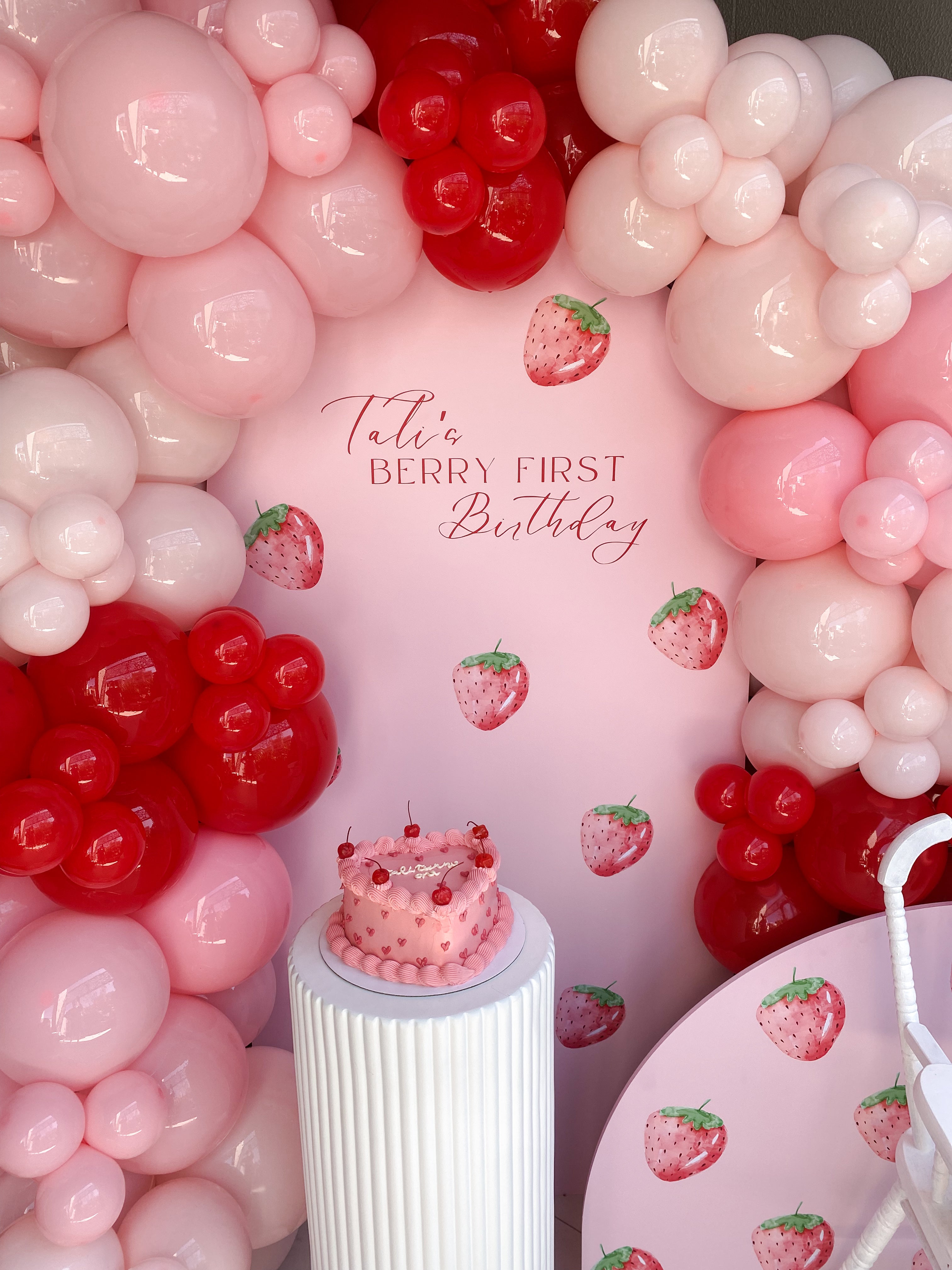 Berry-themed party backdrop with balloons and vinyl signage for first birthday celebration